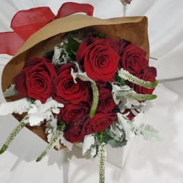 Bouquet of red roses with white filler flowers wrapped in brown paper and red ribbon