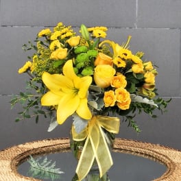Yellow floral arrangement in a glass vase with a ribbon
