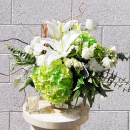 White lilies and green hydrangeas in a glass vase with a candle beside it