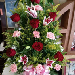 Tall basket arrangement of red roses, pink lilies, and carnations with a pink ribbon