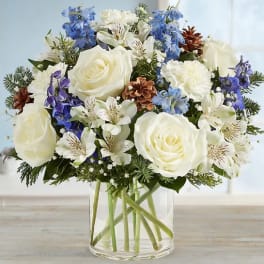 White roses and blue flowers arranged in a clear glass vase