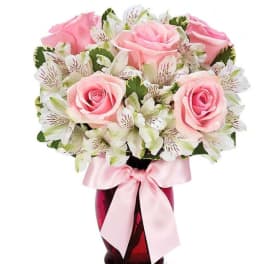 Pink roses and white alstroemeria in a red glass vase with a pink ribbon