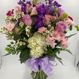 Mixed pink and purple bouquet in a clear glass vase with a lavender ribbon