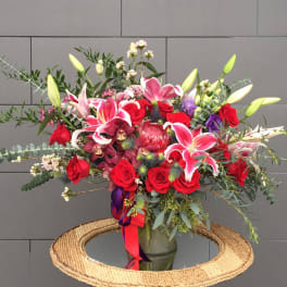 Large mixed bouquet of red roses, pink lilies, and orchids in a glass vase