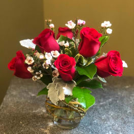 Red roses arranged in a clear glass vase with small white filler flowers.