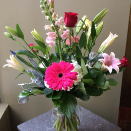 Mixed bouquet with pink gerbera, roses, lilies, and snapdragons in a glass vase