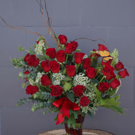 Red roses arranged in a glass vase with a red ribbon and butterfly accent