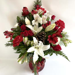 Red and white floral arrangement in a red vase with pinecones