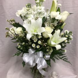 White lilies and roses in a glass vase with a white ribbon