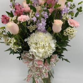 Mixed pink and lavender bouquet in a glass vase with a floral ribbon