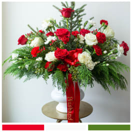 Red and white rose arrangement in a white vase with a red ribbon