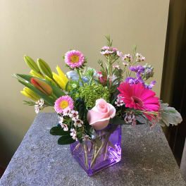 Mixed bouquet with pink rose, gerbera daisies, and lilies in a purple glass vase