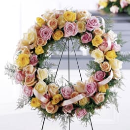 Circular wreath of pastel roses on a stand with ribbon accents