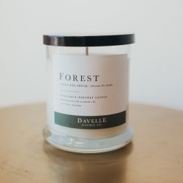 Glass jar candle with a black lid and forest label