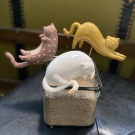 Three ceramic cat figurines rest on a glass container filled with sand.