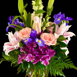 Mixed bouquet with pink roses, lilies, purple irises, and alstroemeria in a glass vase