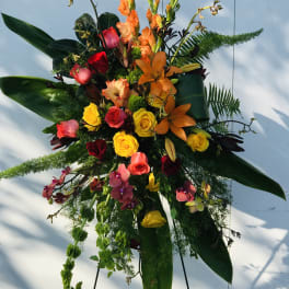 Tall mixed floral spray with roses, lilies, orchids, and orange blooms