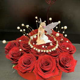 Red rose arrangement with a fairy figurine and pearl accents in a red box