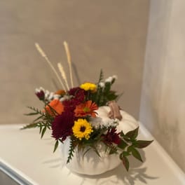 Small floral arrangement in a white pumpkin container with mixed blooms