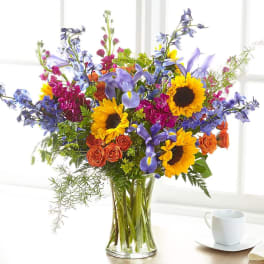 Mixed bouquet of sunflowers, irises, roses, and blue flowers in a glass vase