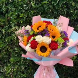 Bouquet of sunflowers, red and white roses, and purple filler flowers wrapped in pink paper