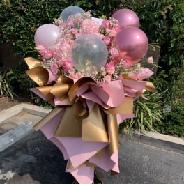 Pink floral arrangement with balloons and metallic wrapping on a stand