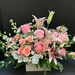 Pink roses and lilies arranged in a white box with greenery