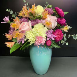 Mixed bouquet in a turquoise vase with pink, purple, and peach blooms