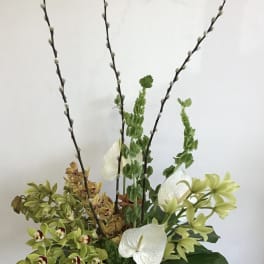 Tall floral arrangement with orchids and white anthuriums in a green vase