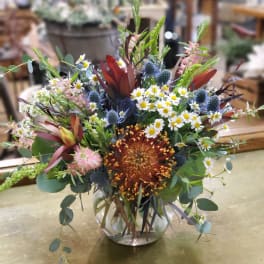 Mixed bouquet in a clear glass vase with daisies and spiky blue flowers