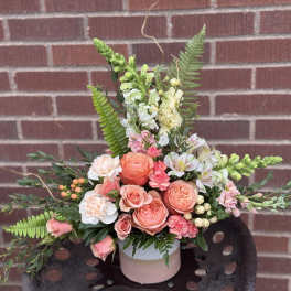 Peach and pink floral arrangement in a pink vase with fern accents