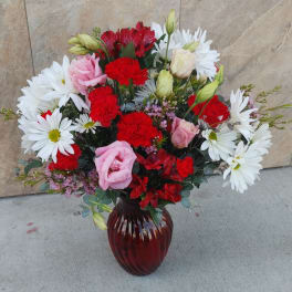 Bouquet of red and pink flowers with white daisies in a red glass vase