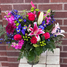 Mixed bouquet of pink roses, lilies, and blue flowers in a glass vase