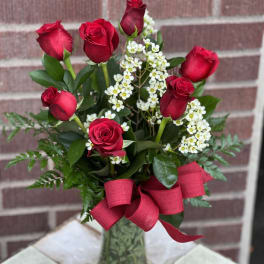 Red roses with white filler flowers in a glass vase and red ribbon
