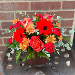 Mixed bouquet of red, coral, and peach flowers in a brown container