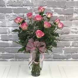 Pink roses arranged in a clear glass vase with a pink ribbon bow