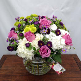 Pink roses and white hydrangeas in a clear glass vase with purple and green accents