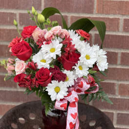 Bouquet of red roses and white daisies in a red vase with a heart ribbon