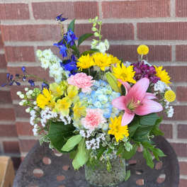 Mixed bouquet in a glass vase with pink lily, blue hydrangea, and yellow daisies