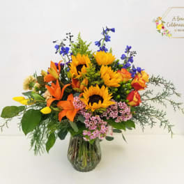 Mixed bouquet with sunflowers, lilies, roses, and blue flowers in a glass vase