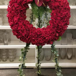 Heart-shaped red rose wreath on a standing easel with anthuriums and fern