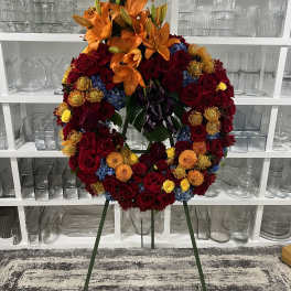 Large floral wreath on a stand with orange lilies and red roses