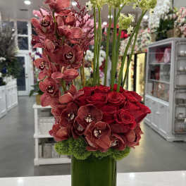 Red roses and orchids arranged in a tall green vase