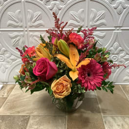 Mixed bouquet of pink, orange, and yellow flowers in a glass vase