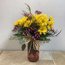 Yellow daisy bouquet in a brown glass vase with pink filler flowers