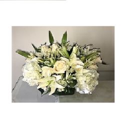 Low white arrangement of roses, lilies, and hydrangeas in a rectangular glass vase