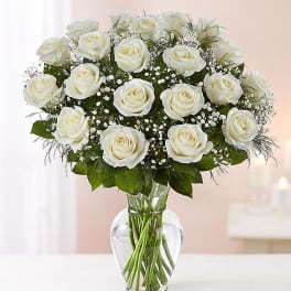 Arrangement of white roses with filler flowers in a clear glass vase