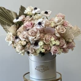 Blush and cream roses arranged in a round hatbox with dried accents