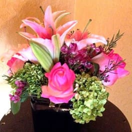 Compact arrangement of pink lilies and roses with green hydrangeas in a black square vase