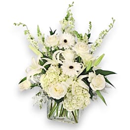 White floral arrangement in a clear square vase with roses, lilies, and daisies